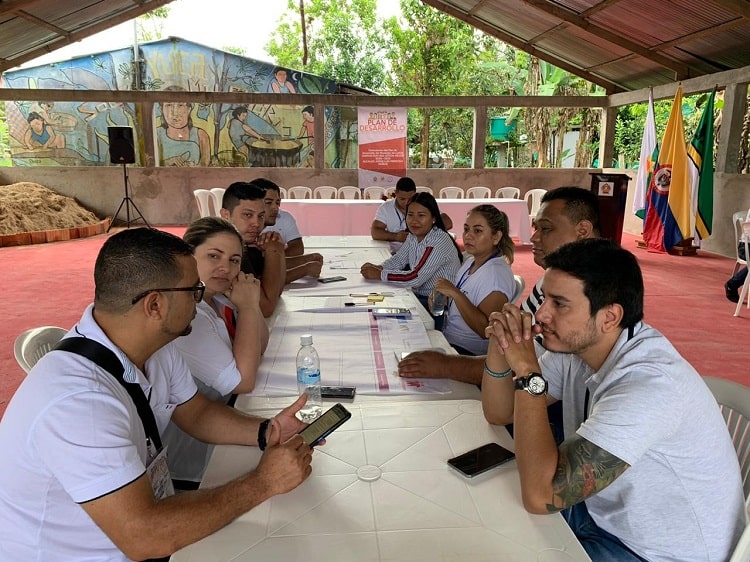 Grupo de personas sentadas a ambos lados de una mesa, en una región de Colombia