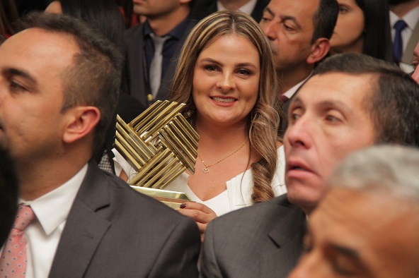 Mujer entre el público con el trofeo del Premio Nacional de Alta Gerencia, sonriendo a la cámara