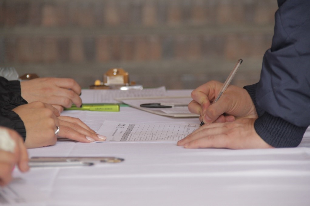 Se observan sobre una mesa, las manos de una persona diligenciado un formulario