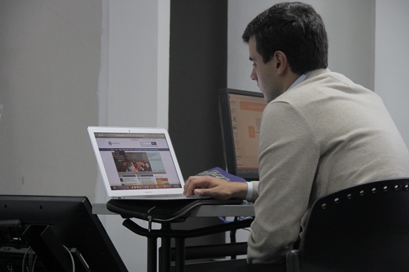 Hombre sentado mirando frente a la pantalla de un computador que está encendido 
