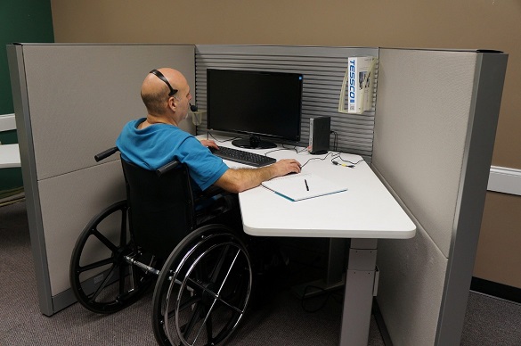 Hombre en silla de ruedas, en un puesto de trabajo, laborando frente a un computador