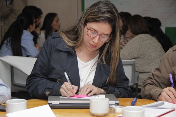 Primer plano de una mujer con gafas, sentada y escribiendo con un esfero sobre un papel