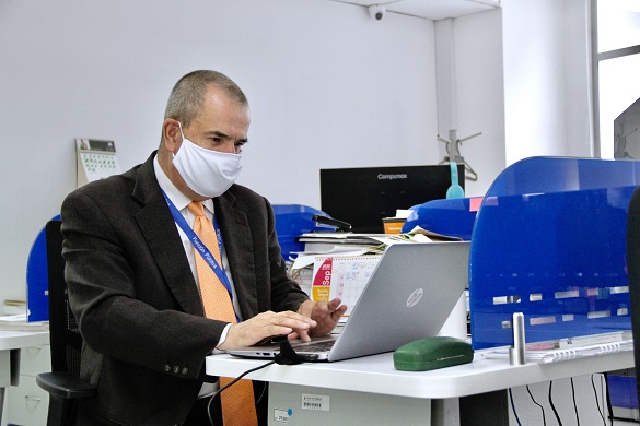 Hombre con tapabocas, en una estación de trabajo escribiendo en un computador portátil