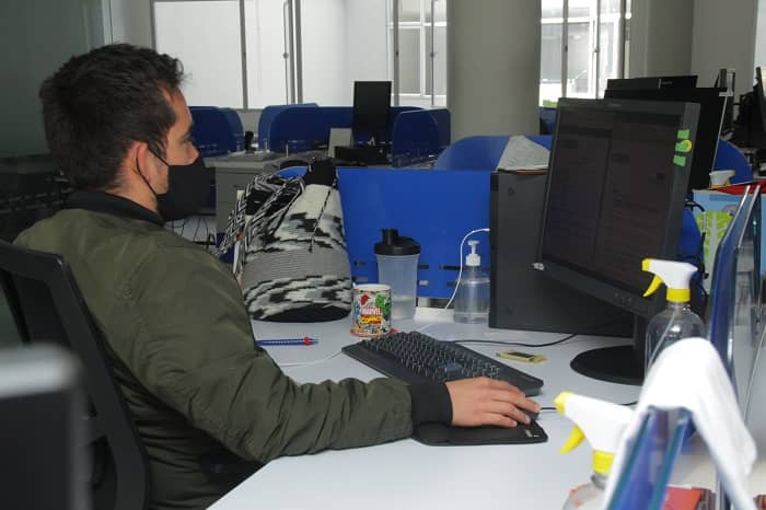 Hombre con tapabocas laborando en un computador en un puesto de trabajo
