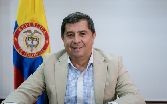 Director de Función Pública, César Augusto Manrique Soacha, sonríe a cámara con la bandera de Colombia en el fondo