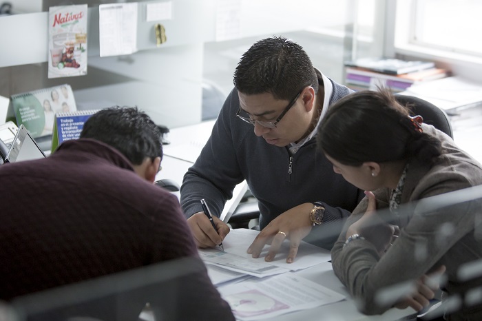 Imagen de tres personas, dos hombres y una mujer, revisando un documento en un puesto de trabajo