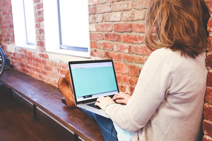 Mujer sentada sobre una banca con un computador portátil en sus piernas
