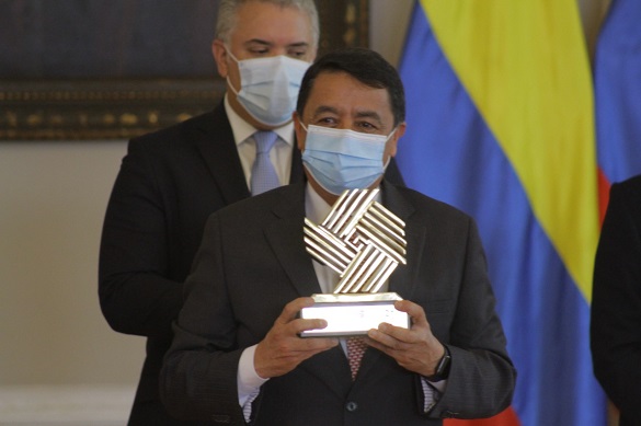 Un hombre con tapabocas sosteniendo entre sus manos el trofeo que entrega el Premio Nacional de Ala Gerencia